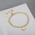 Detailed macro view of a gold-toned heart pendant on a Cuban link chain anklet. - Gold