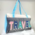 Detail of travel bag with colorful embroidered TRAVEL lettering on grey fabric. - Travel