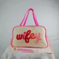 Detailed view of cream travel bag with colorful fuzzy 'wifey' embroidery and pink accents - WIFEY