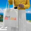 Detail view of white canvas tote bag with 'blessed mama' print used by a person outdoors. - Style 2