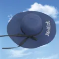 Close-up of blue straw sun hat with black bow and embroidered Melilot lettering - One Size / Navy Blue