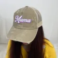 Detailed view of the distressed khaki ponytail trucker hat featuring a purple Mama print - Beige