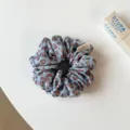 Gros plan d'un chouchou à cheveux en satin à motif léopard bleu et marron avec étiquette. - Petit Chouchou Léopard Bleu