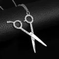 Close-up of silver-toned hairstylist scissor pendant on black textured leather surface. - Silver