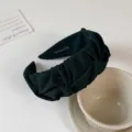 Detailed view of the dark green pleated fabric headband, showcasing fine texture and handmade label. - Dark Green