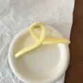 Primo piano di dettaglio di una elegante molletta per capelli in acrilico giallo su piatto. - Stile Incrociato Giallo