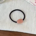 Detail shot of a black hair tie with a pink polka dot oval accent on textured fabric. - Pink