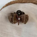 Close-up of a brown plaid hair claw clip with a bow and rhinestone center for chic hairstyles. - Dark Coffee