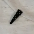 Detail shot of black polka dot hair clip on textured fabric, ideal for stylish daily hairstyles. - Triangle Clip / Black