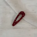 Close-up detail of a dark red polka dot snap hair clip with fabric wrap and metal base. - Waterdrop Hollow / Red