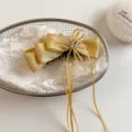 Close-up of gold satin bow hair clip with ribbons and rhinestone detail in a wire basket. - 13cm / Yellow