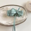 Detail shot of light blue satin bow hair clip with rhinestone and long ribbons in wire basket. - 11cm / Green