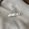 Detailaufnahme einer silbernen, metallischen Wellen-Haarspange mit eleganter Textur und Design. - Welle (Mattweiß)