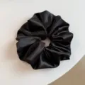 Detailopname van een klassieke zwarte satijnen haarelastiek, elegant glanzend haaraccessoire. - Zwart
