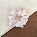 Detail shot of a sweet Korean style pink polka dot scrunchie with metallic charm. - Cream Polka Dot