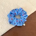 Close up of a blue satin hair scrunchie featuring cute red heart prints and a tiny metal tag. - Deep Blue Heart Pattern