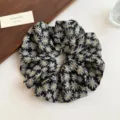 Close-up detail of black floral print hair scrunchie with cute white daisies, soft fabric design. - Black