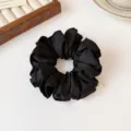 Gedetailleerd uitzicht van elegante zwarte stoffen haarrekkertje met schattige metalen bedel. - Zwart
