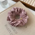Rosa plissiertes Haargummi mit edlem Metallanhänger, stilvolles Stoff-Haar-Accessoire im Detail. - Rosa