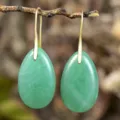 Close-up detail of natural green aventurine teardrop pendant earrings hanging on a rustic branch. - Green Aventurine