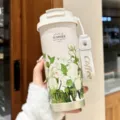 Detail view of the white floral insulated coffee tumbler showing seasonal garden print and lanyard. - Garden Series Green
