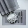 Detail shot of grey woven PVC placemat with elegant black and white checkered plate and cutlery set. - Silver-Gray Single Frame