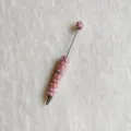 Detailansicht eines DIY-Perlenkugelschreibers mit rosa Perlen, Strasssteinen und Metallstift. - Rosa