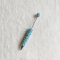 Nahaufnahme des DIY Perlenkugelschreibers dekoriert mit blauen Perlen und funkelnden Kristallen. - Seeblau