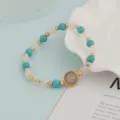 Close-up detail of turquoise and white bead bracelet with elegant gold tone metal charms. - Turquoise and White Premium Style