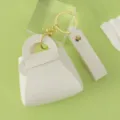 Mini white leather handbag keychain with gold hardware, detailed close-up shot of small purse charm. - White