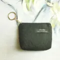 Detailed view of a black textured mini coin purse featuring a gold keychain and fabric label. - 12*2.5*8.5CM / Black