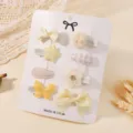 Close-up of yellow hair clip set with bow and star designs on display card - 7 Pieces / Yellow/Beige Set (8D)