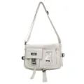 Front detail view of a cream nylon messenger bag featuring multiple utility pockets. - Messenger Bag (Includes Badges) / White