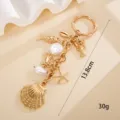 Detailed view of a gold ocean-themed keychain featuring shell and crab charms with size info - 贝壳加小鱼挂件 / Gold