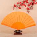 Orange plastic folding fan, classic solid color variant, elegant dancing accessory. - Orange