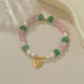 Nahaufnahme des Perlen- und Kristallarmbands mit goldenem Herzanhänger für elegante Modeschmuck. - Süßwasserperle Rosenquarz & Grüner Stein (B4260)