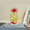 Detailed view of a glowing red artificial rose inside a clear glass dome with fairy lights. - Acrylic / Red