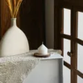 Close-up shot of a white striped cone pillar scented candle styled on wooden slice coaster. - White Pointed Top Ribbed (5*5)