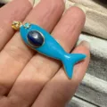 Nahaufnahme des blauen Emaillenfisch-Anhängers mit Goldrand und Edelsteineinlage. - Hellblau