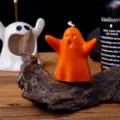 Close-up detail shot of the cute orange ghost shaped scented candle on rustic wooden decor. - Passionate Hugging Ghost / Orange