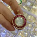 Gold-plated circular pendant featuring mother-of-pearl carved figure with red cubic zirconia - Red