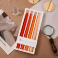 Detailansicht von duftenden Stabkerzen mit Farbverlauf in weißer Geschenkbox mit warmen Requisiten. - Farbverlauf Orange (Orangefarben)