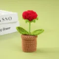 Primer plano de rosa de ganchillo hecha a mano en maceta, linda flor tejida para escritorio. - Rojo