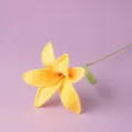 Close up detail of a handcrafted yellow crochet lily flower with green stem and leaf. - Yellow