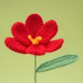 Handmade crochet red flower detail closeup, showing neat stitches, yellow center and green leaf. - Red