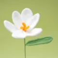 Handcrafted white crochet flower detail showing delicate petals, yellow stamen, and green leaf. - White