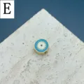 Gros plan détaillé sur la perle ronde émaillée œil maléfique, accessoire bijou DIY doré. - Lettre E