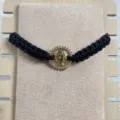 Dettaglio in primo piano del bracciale in corda intrecciata nera con ciondolo Guadalupe dorato. - Nero
