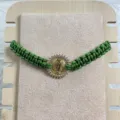 Close-up detail of green woven rope bracelet featuring golden Guadalupe pendant with cubic zirconia. - Dark Green