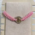 Adjustable pink woven cord bracelet featuring a gold tone Guadalupe pendant with clear zirconia. - Pink